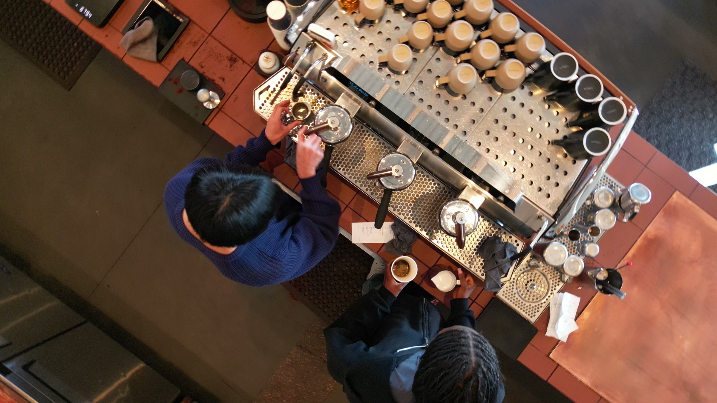 The espresso bar from directly above: the machine, the cups, two baristas at work