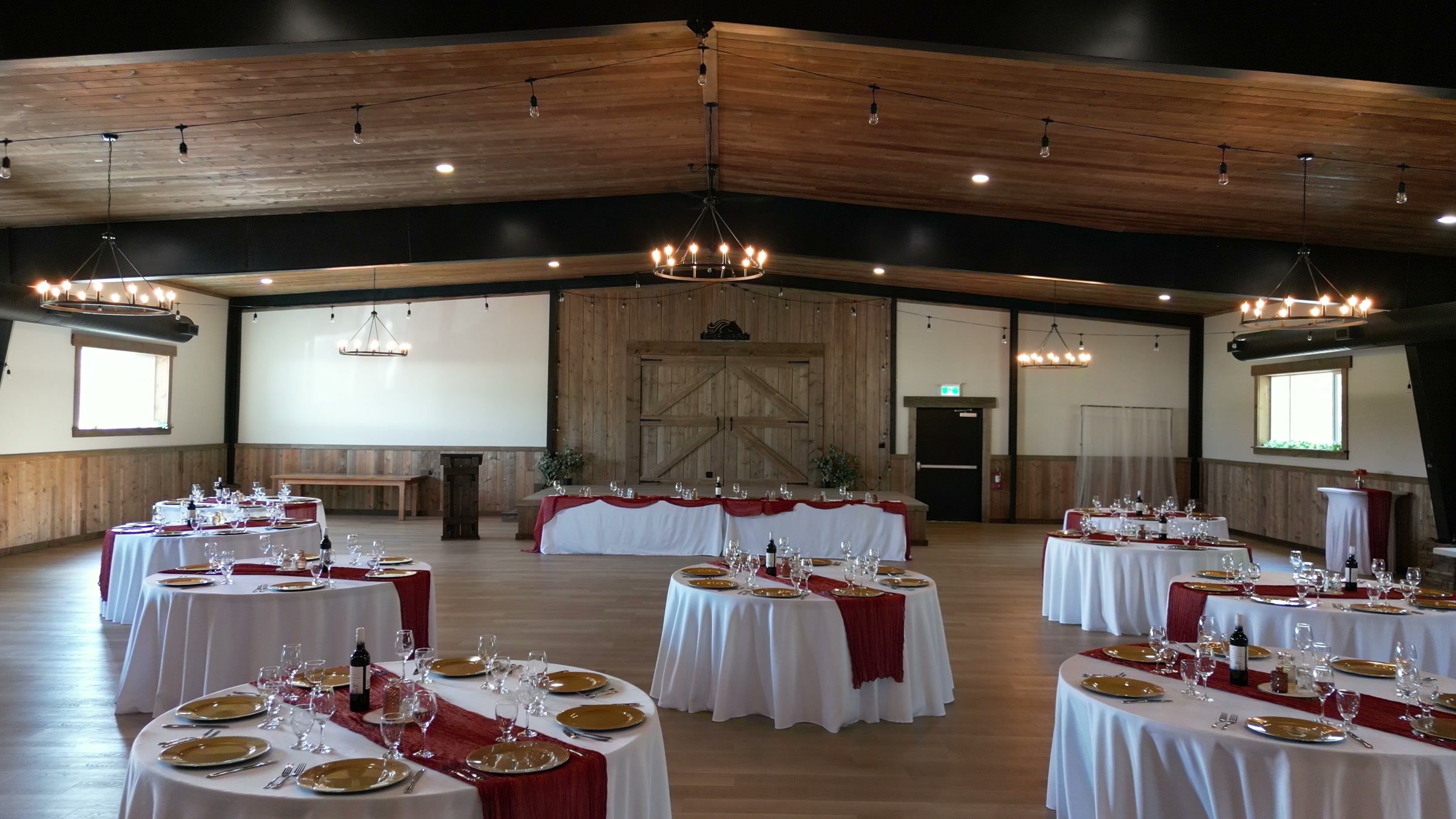 The wedding hall set for a reception: round tables, a chandelier, timber walls